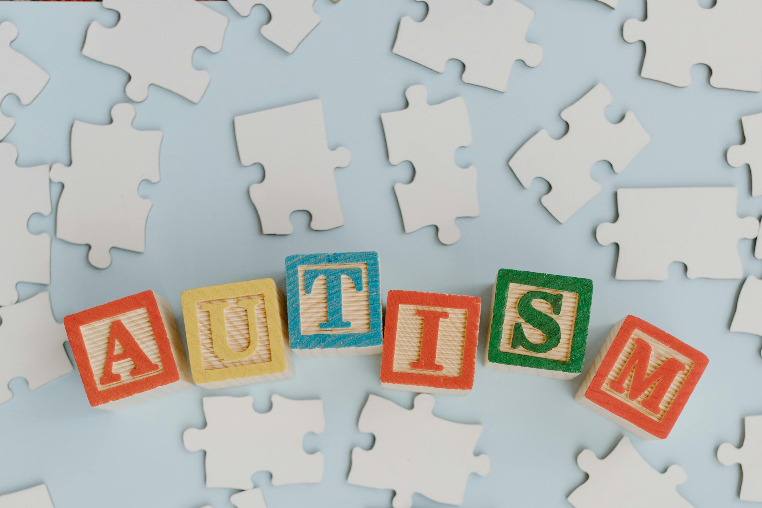cubes en bois formant le mot AUTISM sur fond de puzzle